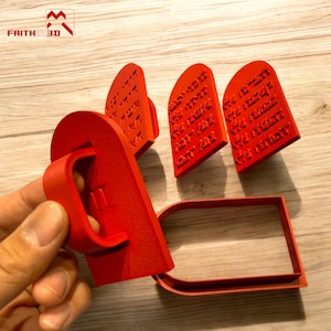 May include: Red plastic cookie cutters shaped like the Ten Commandments tablets and an archway. The tablets have Hebrew text on them.