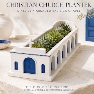 Peut inclure: Une jardinière rectangulaire blanche en forme de chapelle basilique à arcades avec des portes et des fenêtres bleues. La structure présente une croix sur la façade avant et contient diverses plantes succulentes vertes.