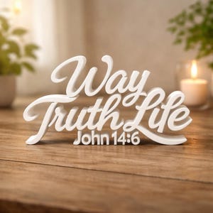 May include: White decorative sign with the words "Way Truth Life" in a cursive font. The text "John 14:6" is below the words. The sign is on a wooden surface.