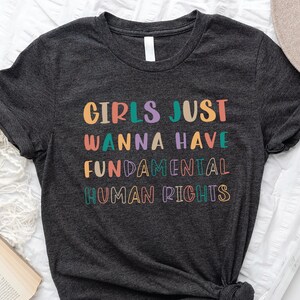 May include: A dark grey t-shirt with the text "Girls Just Wanna Have Fundamental Human Rights" printed in colourful letters.