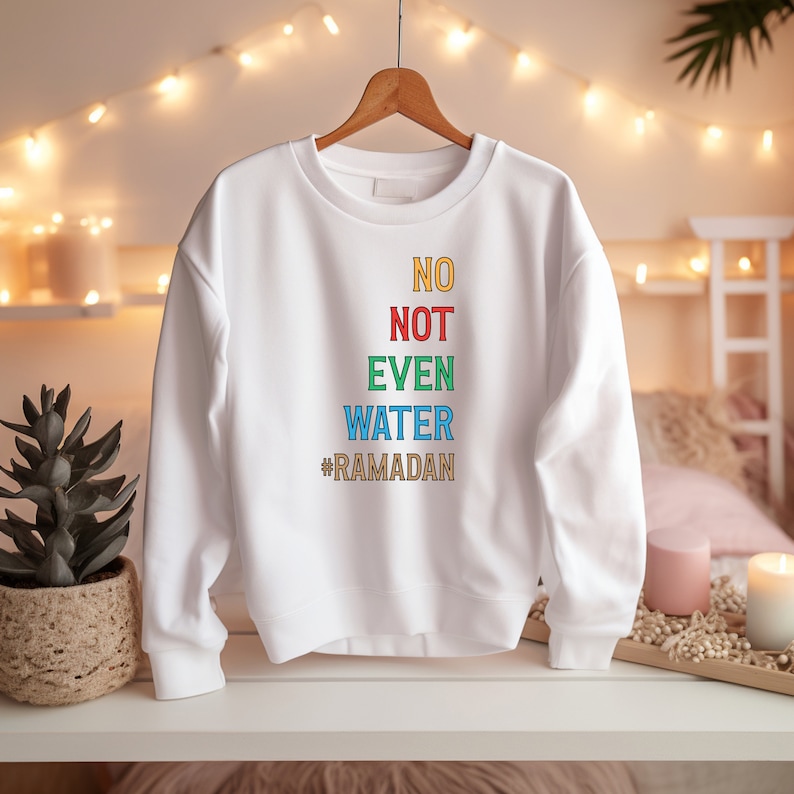 Op de afbeelding: Witte trui met de tekst "NO NOT EVEN WATER #RAMADAN" in regenboogkleuren.