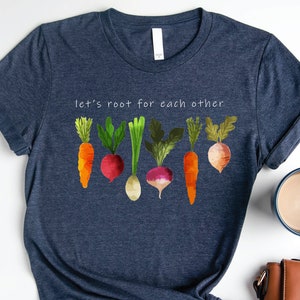 May include: A navy blue t-shirt with the text "let's root for each other" and a graphic of colourful vegetables, including carrots, radishes, and turnips.