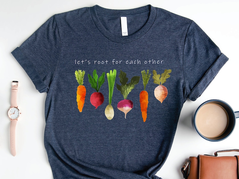 May include: A navy blue t-shirt with the text "let's root for each other" and a graphic of colourful vegetables, including carrots, radishes, and turnips.