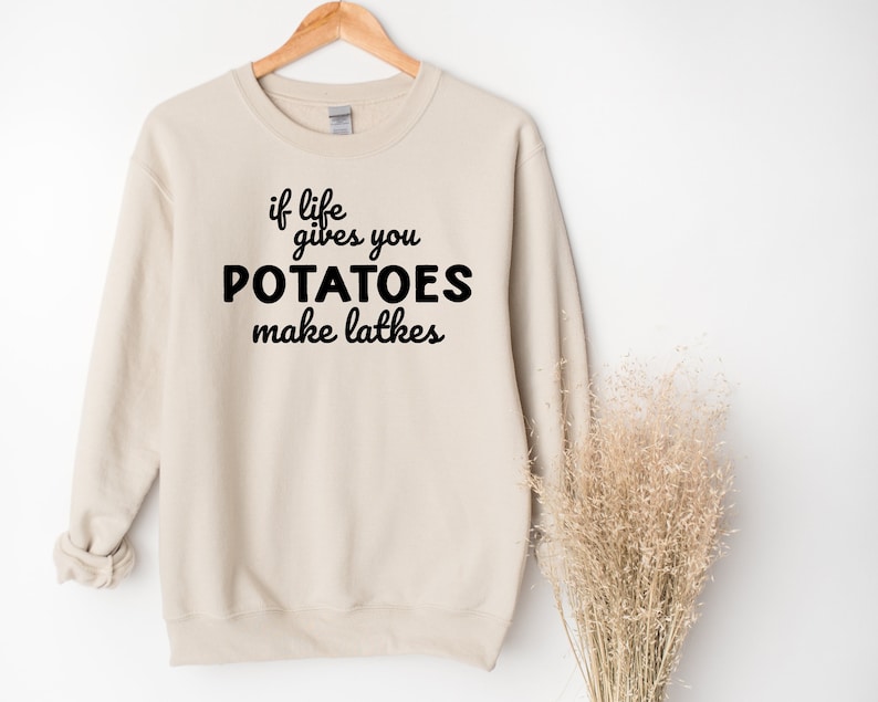 Peut inclure: Un sweat-shirt beige avec le texte "if life gives you POTATOES make latkes" imprim&eacute; en noir.