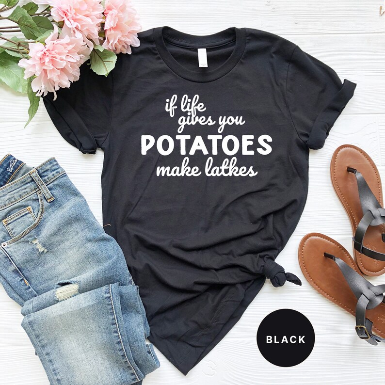 Peut inclure: T-shirt noir avec un texte blanc qui dit "if life gives you potatoes make latkes". Le t-shirt est pos&eacute; &agrave; plat sur une surface blanche avec un jean bleu et des sandales marrons.