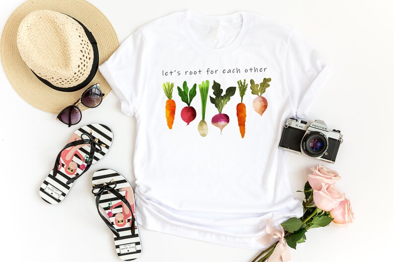 May include: White t-shirt with the text "Let's root for each other" and a watercolour illustration of carrots, radishes, and turnips.