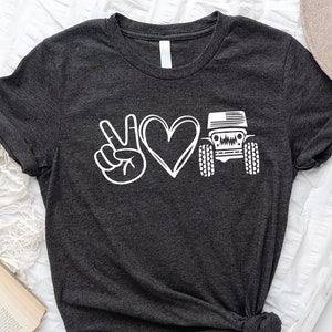 May include: A dark gray t-shirt with a white peace sign, heart, and a Jeep silhouette. The Jeep has an American flag on the hood.