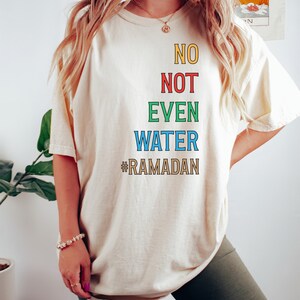 Op de afbeelding: Een wit T-shirt met de tekst "NO NOT EVEN WATER #RAMADAN" in kleurrijke letters.