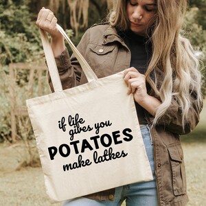 Peut inclure: Un sac fourre-tout en toile blanche avec du texte noir qui dit "Si la vie vous donne des pommes de terre, faites des latkes".