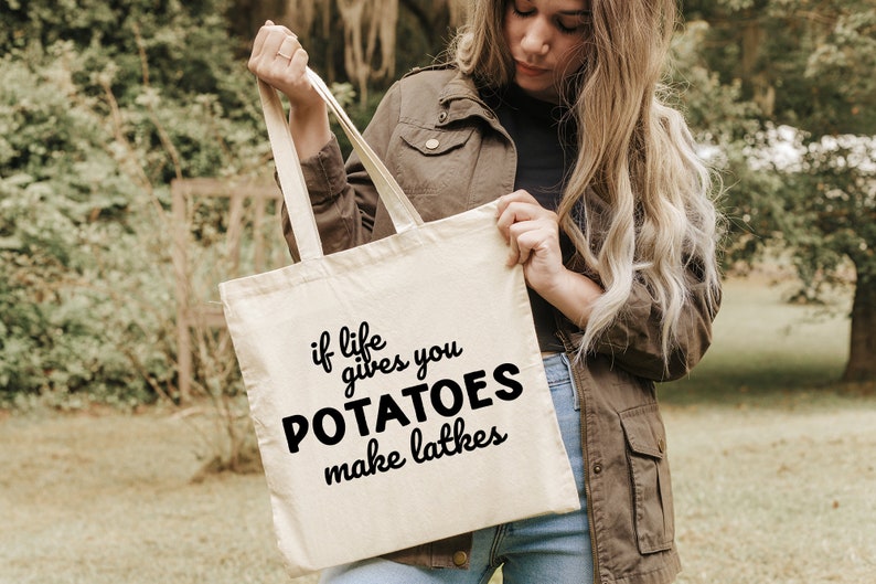 Peut inclure: Un sac fourre-tout en toile blanche avec du texte noir qui dit "Si la vie vous donne des pommes de terre, faites des latkes".