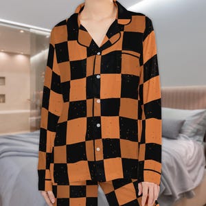 May include: A long-sleeved pyjama top and matching trousers set featuring a black and burnt orange checkered pattern with a subtle distressed texture. The top includes a notched collar, a front button-down closure, and a single chest pocket.