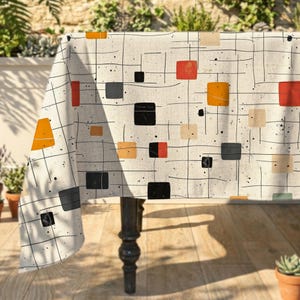 Peut inclure: Une nappe en tissu crème ornée d'un quadrillage de fines lignes noires et de taches noires éparpillées. Le motif présente divers carrés et rectangles pleins dans des tons orange, rouge, noir et beige répartis sur toute la surface.