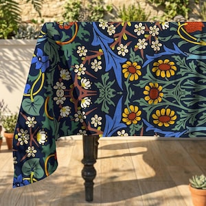 May include: A navy blue tablecloth with a floral design, showcasing yellow, white, and blue flowers, green leaves, and brown stems. The cloth is draped over a dark wooden table, offering a vibrant and decorative touch.