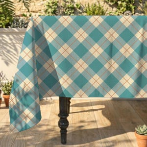 May include: A teal and cream plaid tablecloth with a red grid pattern. The tablecloth is draped over a dark wooden table, creating a stylish and decorative look. The pattern is a classic argyle design, suitable for various occasions.