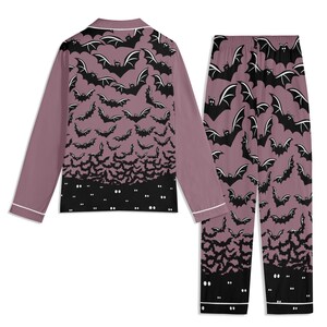 May include: A long-sleeve button-down pajama top and matching pajama pants in a dusty mauve color. The set features an all-over print of black bats, transitioning into a solid black hemline at the bottom with small white glowing eyes.