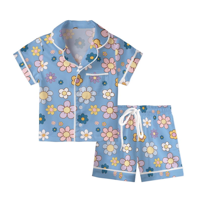 Puede incluir: Conjunto de pijama azul claro con estampado floral. La parte superior de manga corta tiene cuello y botones, y los pantalones cortos tienen cintura con cord&oacute;n. El dise&ntilde;o floral incluye flores rosas, amarillas y blancas.