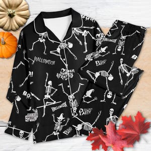 Può includere: Pigiama nero di Halloween con stampa di scheletri bianchi. La maglia a maniche lunghe e i pantaloni presentano scheletri danzanti, le parole "Halloween", "Halloween Party" e "Let's Get Spooky".