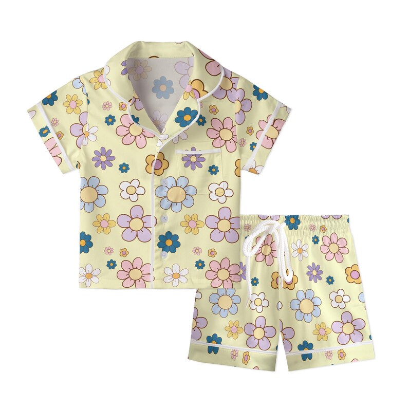 Puede incluir: Un conjunto de pijama de dos piezas con un estampado floral amarillo. El conjunto incluye una camisa de manga corta con botones y bolsillo en el pecho, y pantalones cortos a juego con cintura con cord&oacute;n. El dise&ntilde;o floral incorpora colores pastel como rosa, azul y morado.
