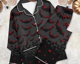 May include: A two-piece pajama set featuring a long-sleeved button-down shirt and matching pants. The fabric is dark gray with a repeating pattern of black bats with red wing outlines. The shirt has white piping along the collar and front.