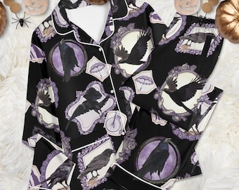 May include: A black pajama set featuring a long-sleeved button-down shirt and matching pants. The fabric displays a repeating pattern of black ravens, ornate purple and white frames, small umbrellas, and bicycles against a dark background.