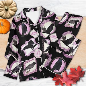 May include: Black pajama set featuring a repeating pattern of black crows in ornate pink frames, umbrellas, and bicycles. The set includes a button-down top with white trim and matching pants. The background is black.