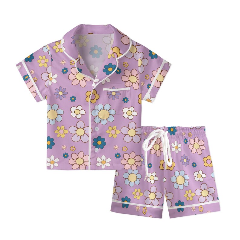 Puede incluir: Un conjunto de pijama lila con un estampado floral en tonos amarillos, azules y rosas. La parte superior de manga corta tiene botones y un bolsillo en el pecho. Los pantalones cortos a juego tienen cintura con cord&oacute;n y ribete blanco.