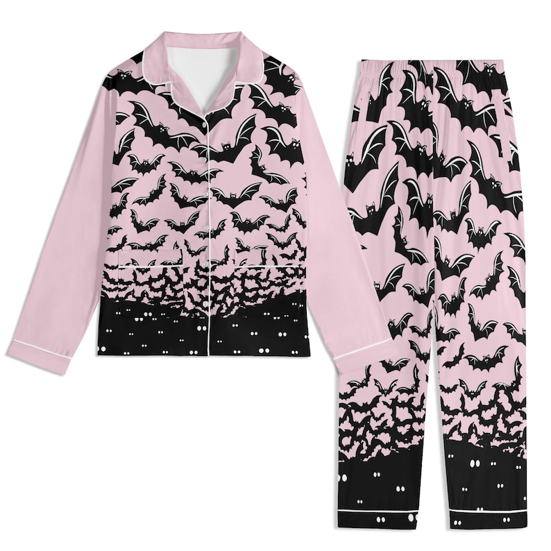 May include: A two-piece pajama set featuring a long-sleeved button-down shirt and matching pants. The fabric is light pink with a repeating black bat pattern that transitions into a solid black hemline featuring small white glowing eyes.