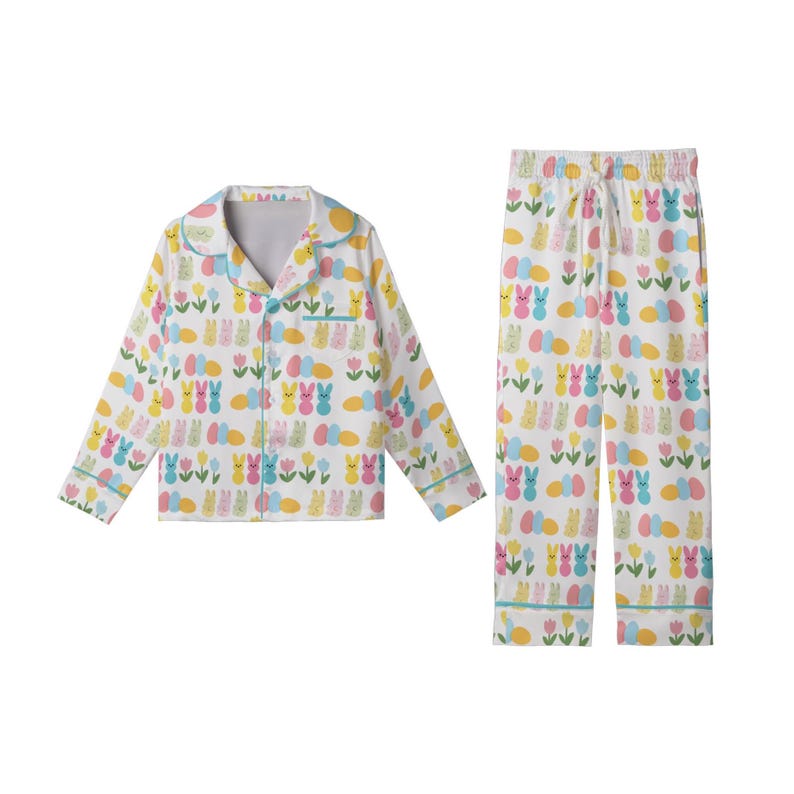May include: White pajama set with a colorful Easter-themed pattern. The set includes a button-down top and pants, both adorned with bunnies, eggs, and flowers in pastel shades of pink, yellow, blue, and green. The trim is light blue.