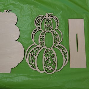 Op de afbeelding: Ongeschilderde houten pompoen uitsparingen voor herfstdecoratie. Inclusief een effen pompoenvorm, een decoratieve pompoen met ingewikkelde uitgesneden ontwerpen en twee rechthoekige stukken met sleuven.
