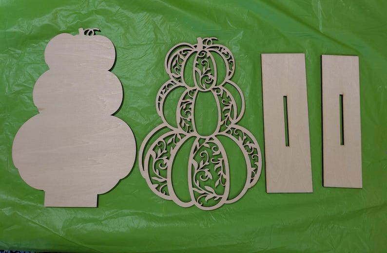 Op de afbeelding: Ongeschilderde houten pompoen uitsparingen voor herfstdecoratie. Inclusief een effen pompoenvorm, een decoratieve pompoen met ingewikkelde uitgesneden ontwerpen en twee rechthoekige stukken met sleuven.