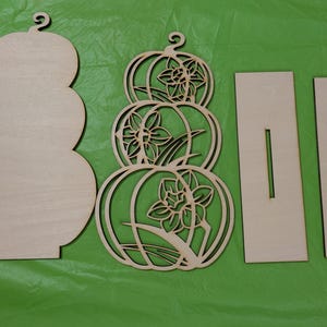 Op de afbeelding: Ongefinished houten pompoenvormige uitsparingen en steunstukken. Een effen pompoenvorm, een decoratieve pompoen met bloemuitsparingen en twee rechthoekige steunen met sleuven. Perfect voor herfst DIY decoratie.
