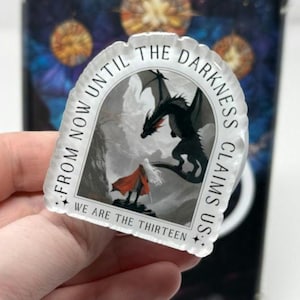 May include: A clear sticker with a fantasy illustration of a black dragon facing a figure in a red cloak. The text around the image reads "FROM NOW UNTIL THE DARKNESS CLAIMS US: WE ARE THE THIRTEEN."