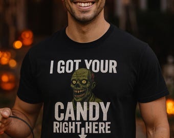 May include: Black t-shirt with the text "I GOT YOUR CANDY RIGHT HERE" and a green zombie graphic. The person in the image is holding an orange jack-o'-lantern bucket. The background is blurred with orange lights.
