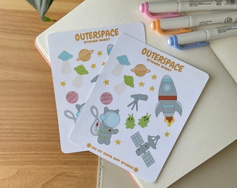 May include: Two sticker sheets with an outer space theme. The sticker sheets are white with a blue and yellow border. The stickers include planets, stars, a rocket, an astronaut, a satellite, and aliens. The text on the sticker sheets reads "Outer Space Sticker Sheet" and "On My Days Off Studio".