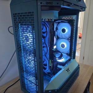 K&ouml;nnte beinhalten: Ein teal-farbenes Computergeh&auml;use mit einer Mesh-Frontplatte und internen Komponenten, die von blauen LED-Leuchten beleuchtet werden. Das Geh&auml;use hat ein einzigartiges, eckiges Design und verf&uuml;gt &uuml;ber mehrere L&uuml;fter.
