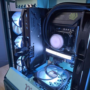 K&ouml;nnte beinhalten: Ein individuell gebautes Computergeh&auml;use in T&uuml;rkis, das interne Komponenten zeigt. Das Bild zeigt eine Grafikkarte mit AMD Radeon- und Gigabyte-Branding, zusammen mit mehreren L&uuml;ftern und LED-Beleuchtung in Blau und Wei&szlig;. Das Geh&auml;use ist offen.