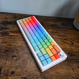 May include: A white mechanical keyboard with rainbow-colored keycaps. The keycaps transition through a spectrum of colors, from blue to red. The keyboard has a silver knob on the side.