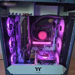 K&ouml;nnte beinhalten: Ein Computergeh&auml;use mit internen Komponenten, die von violetten Lichtern beleuchtet werden. Das Geh&auml;use hat ein Thermaltake-Logo. Zu den Komponenten geh&ouml;ren eine Radeon-Grafikkarte und mehrere L&uuml;fter.