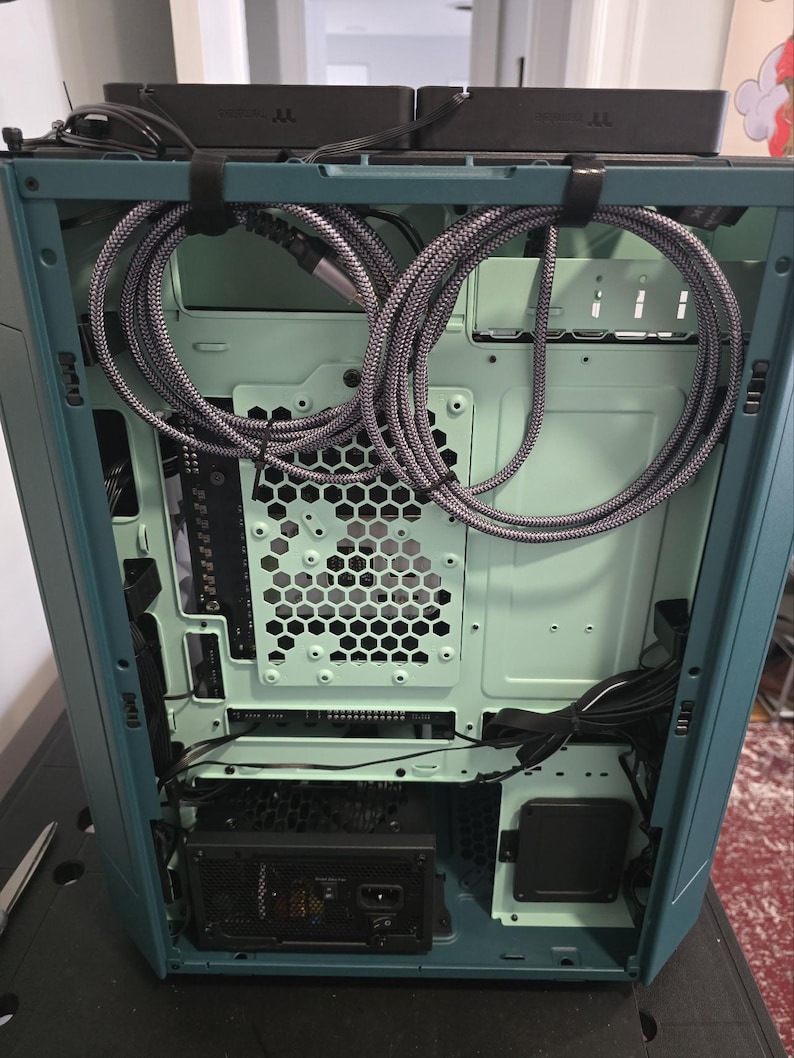 K&ouml;nnte beinhalten: Ein offenes Computergeh&auml;use mit tealfarbenem &Auml;u&szlig;eren und hellgr&uuml;nem Inneren. Geflochtene graue Kabel sind ordentlich im Inneren angeordnet. Ein Netzteil und andere Komponenten sind sichtbar.