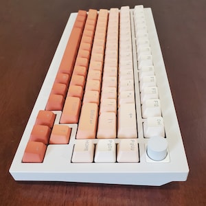 May include: A mechanical keyboard with a white frame and gradient keycaps in shades of orange and white. The keyboard has a volume knob and a variety of function keys. The keycaps are arranged in a standard layout.