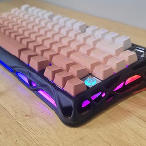 May include: A mechanical keyboard with a gradient keycap design, transitioning from a warm peach to white. The keyboard has a black frame with colorful LED lighting along the edges. The keys are arranged in a standard layout.