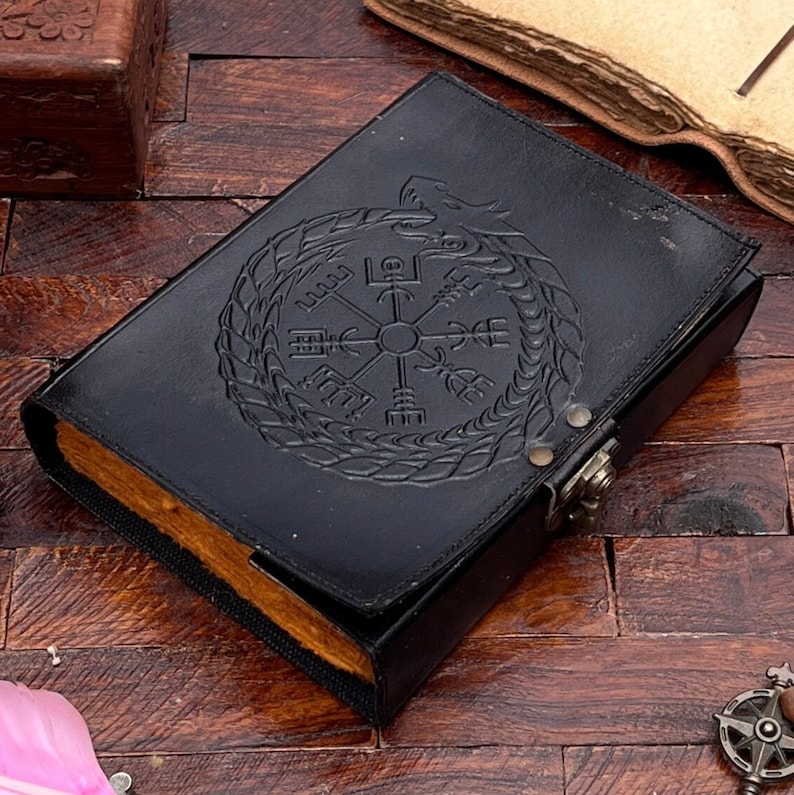 May include: Black leather journal with a compass and dragon design embossed on the cover. The journal has a clasp closure.