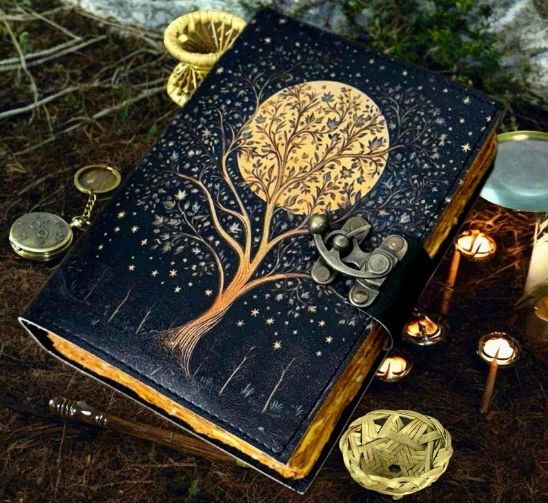 Puede incluir: Un diario de cuero negro con un dise&ntilde;o de &aacute;rbol y luna dorados. El diario tiene un cierre de metal y est&aacute; decorado con estrellas doradas.