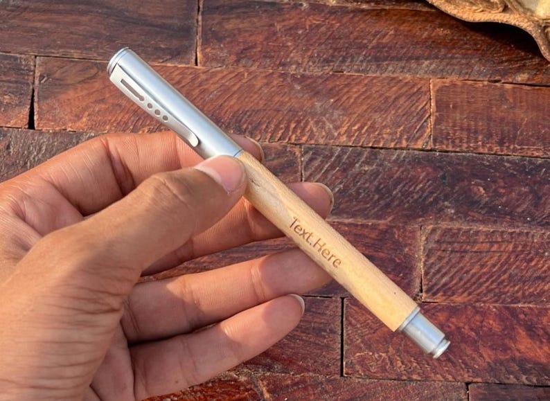 Puede incluir: Un bol&iacute;grafo de madera con una parte superior plateada y una inscripci&oacute;n personalizada que dice "Text Here".