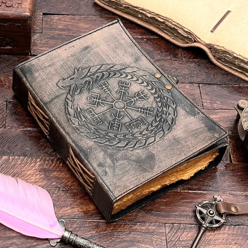 May include: A brown leather journal with a compass and dragon design. The journal has a distressed look and is closed.