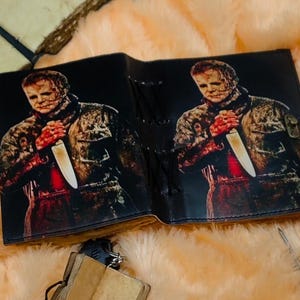 May include: A black leather journal with a graphic print of a horror movie character holding a knife. The journal has a lace-up closure.