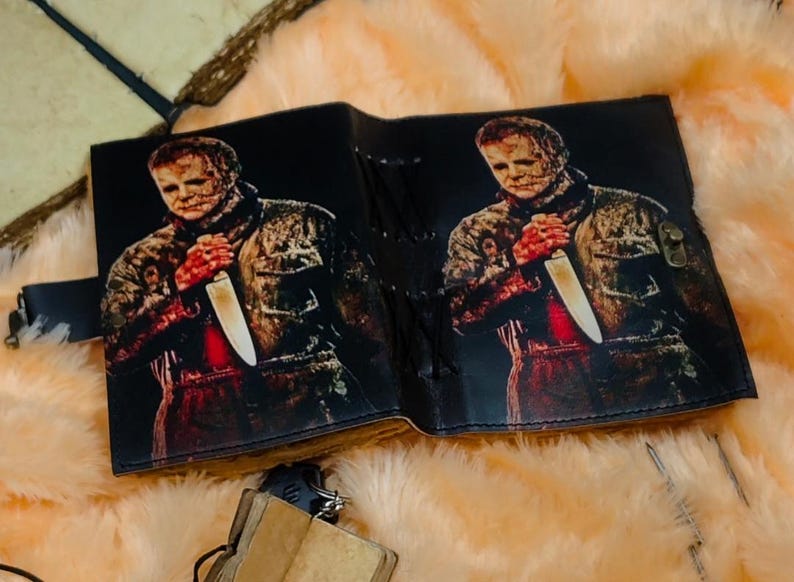 May include: A black leather journal with a graphic print of a horror movie character holding a knife. The journal has a lace-up closure.