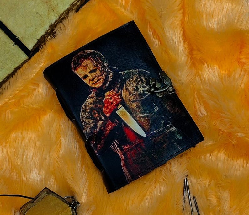 May include: A black leather journal with a graphic of a horror movie character holding a knife. The journal has a metal clasp.