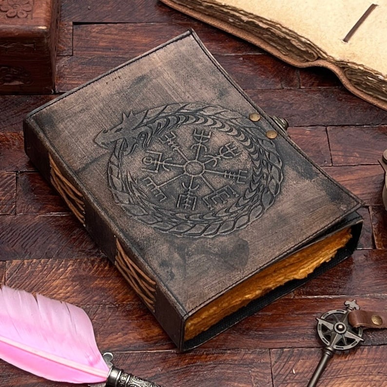 May include: A brown leather journal with a compass and dragon design. The journal has a worn look and is closed.