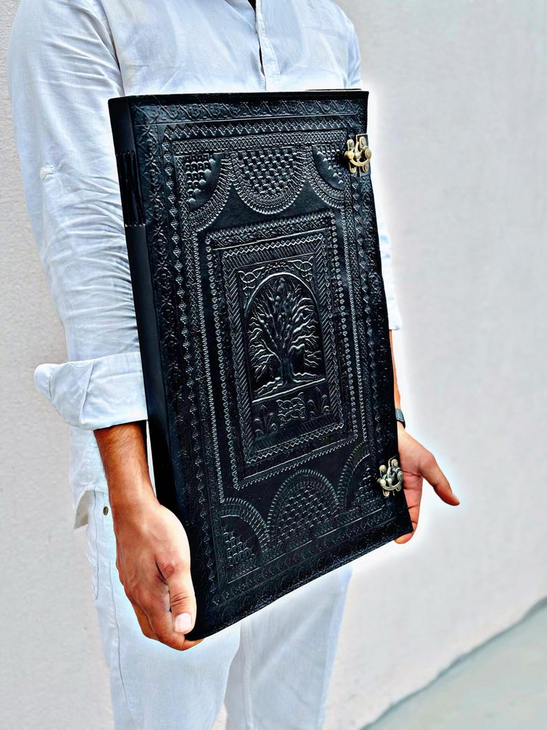 Pode incluir: Di&aacute;rio de couro preto com um design de &aacute;rvore em relevo e fecho de metal decorativo. O di&aacute;rio apresenta padr&otilde;es detalhados e uma superf&iacute;cie texturizada, criando uma est&eacute;tica vintage. Um caderno &uacute;nico para escrever e desenhar.